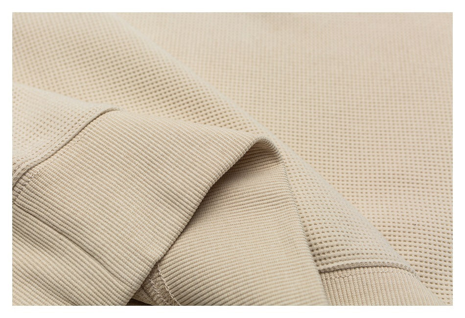 Close-up of beige perforated knit fabric with a ribbed edge and visible stitched seam.