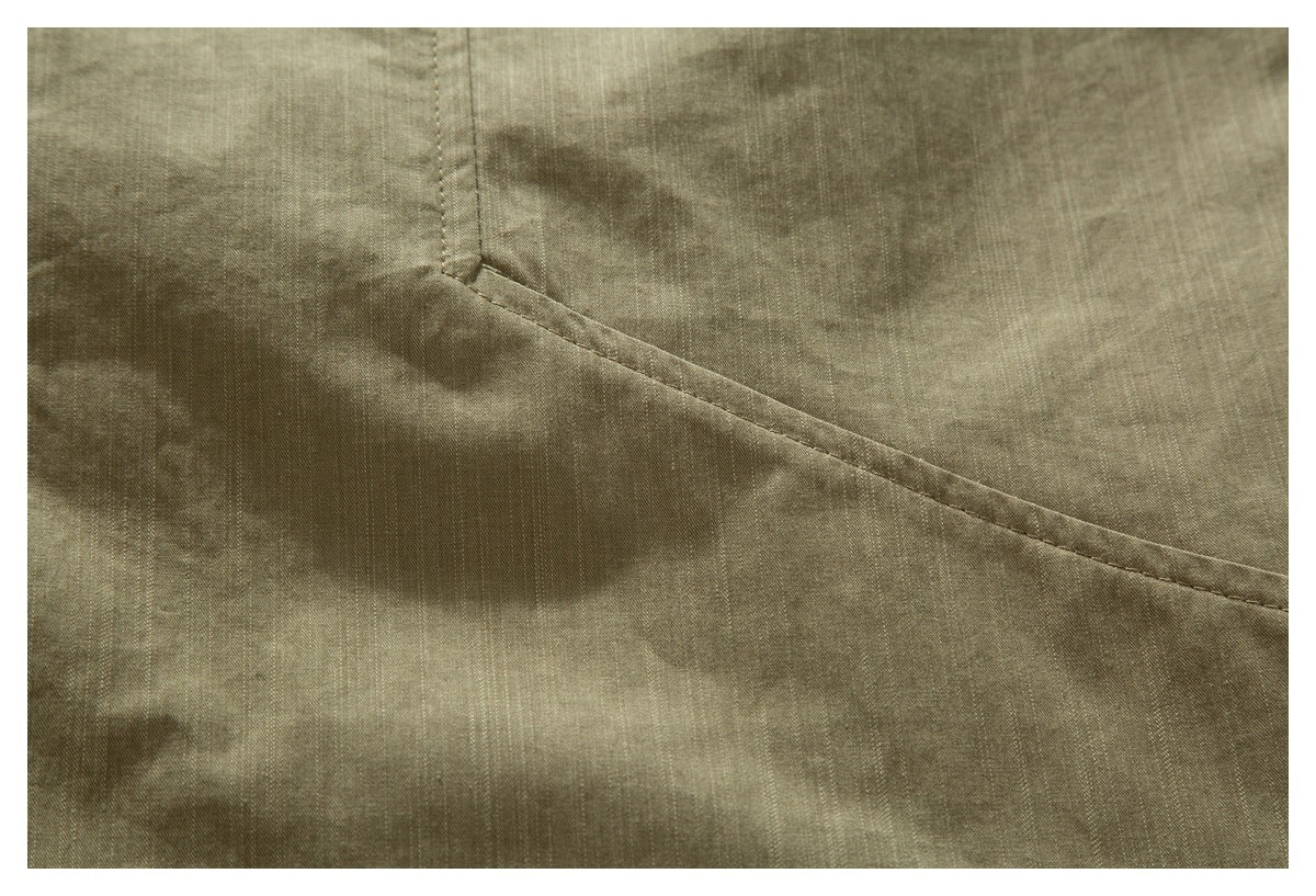 Close-up of an olive-khaki shirt showing a curved stitched pocket edge and fabric texture.