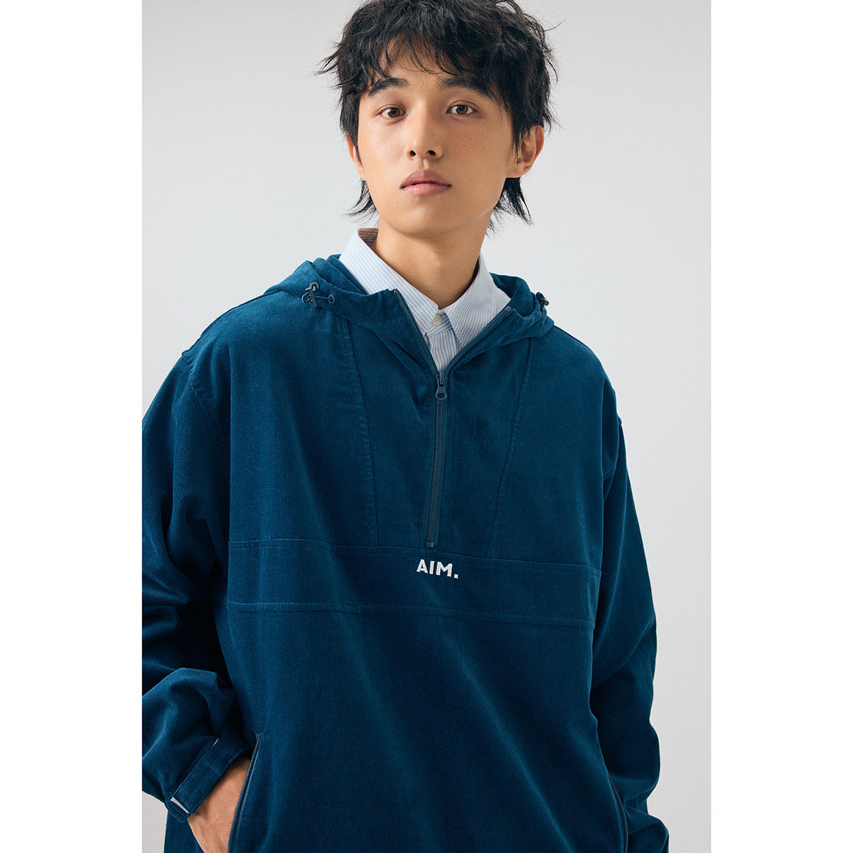 Close view of a model wearing a navy hooded pullover with a short front zip and white AIM chest print.