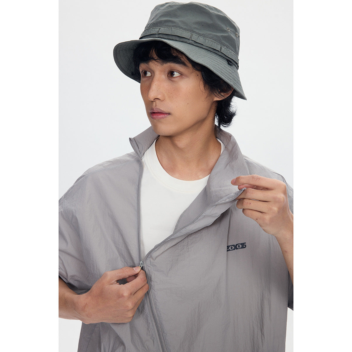 Close-up of the light gray jacket's raised collar, diagonal zipper, and small chest mark.