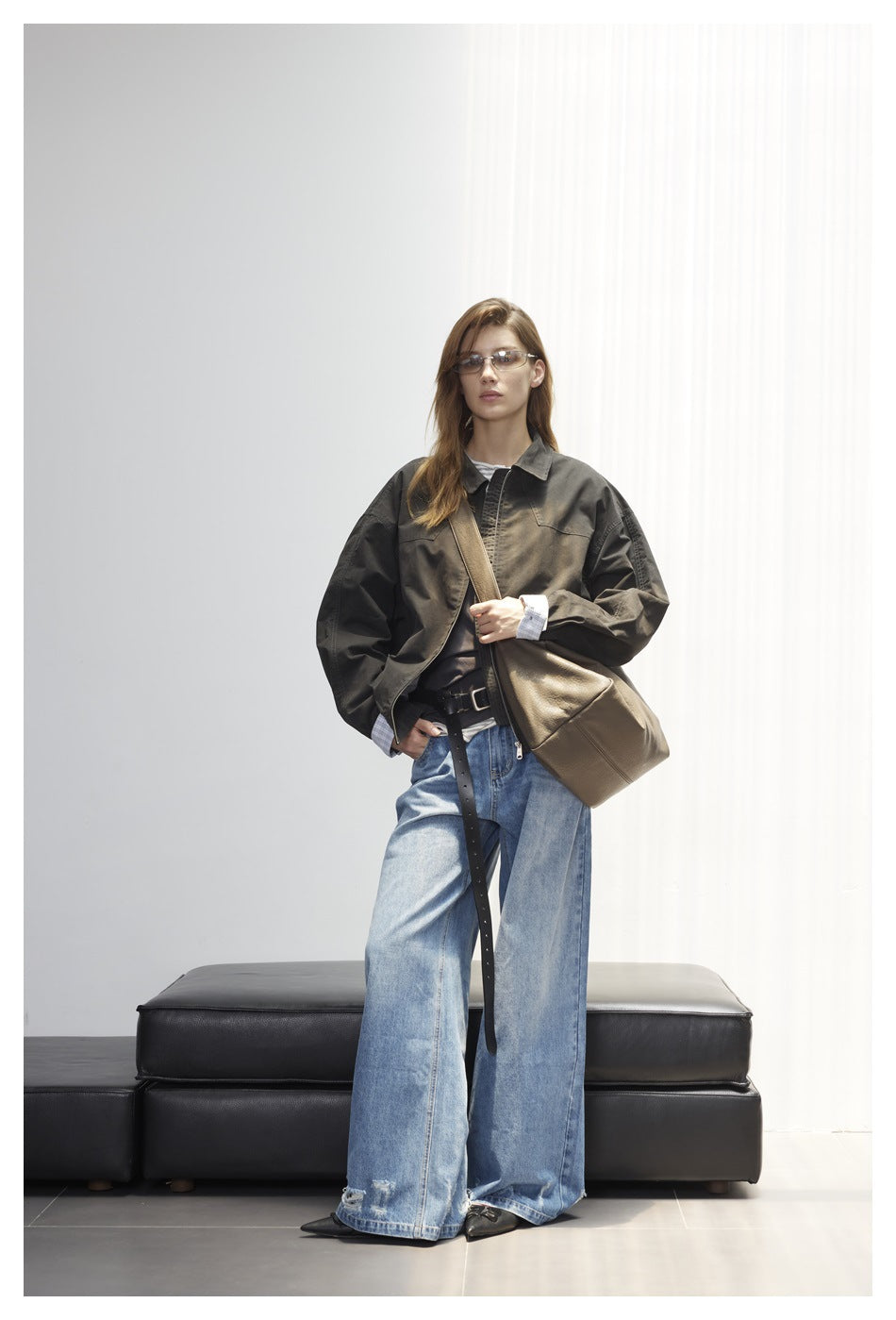 Full-length front view of a model wearing a dark olive oversized jacket with chest pockets and wide-leg blue jeans.