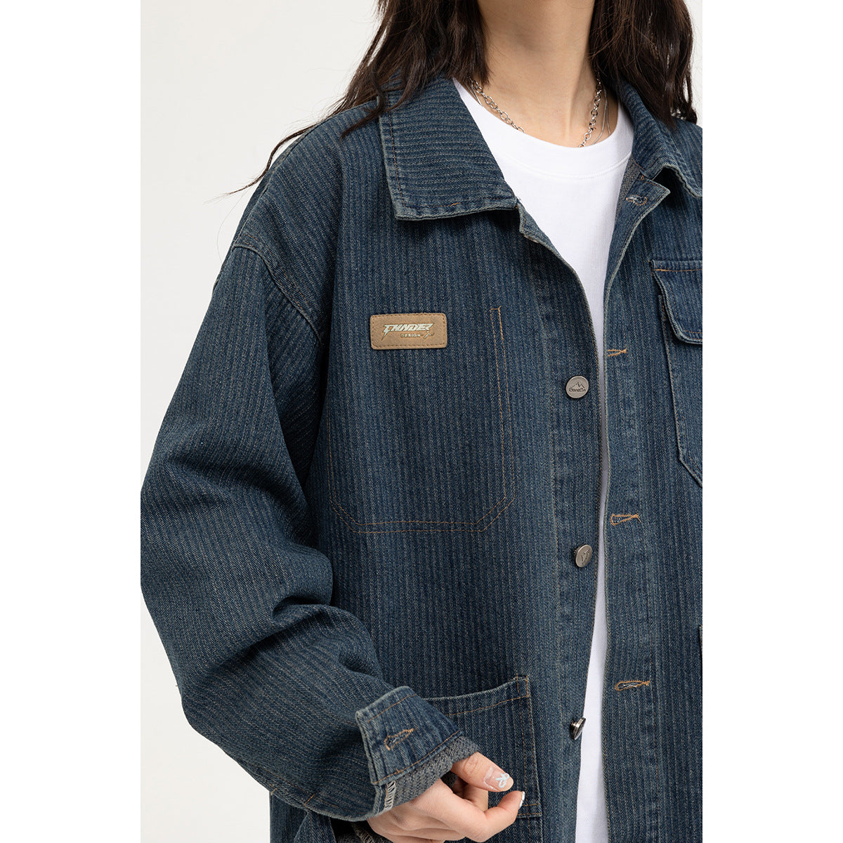 Close-up of a model wearing a dark blue denim jacket, showing its collar, buttons, patch pockets, and chest badge.