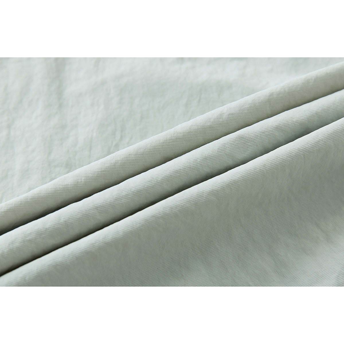 Close-up of pale sage fabric arranged in folds, showing its subtle surface texture.