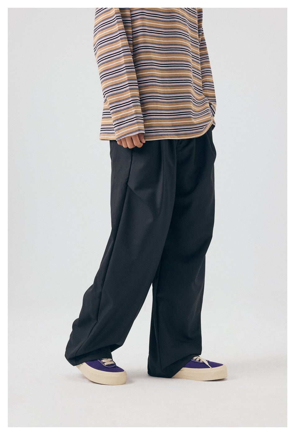 Side-angle view of a model wearing black wide-leg trousers and a tan striped long-sleeve shirt.