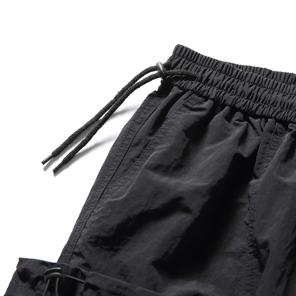 Close-up of black shorts showing the elastic waistband, long drawstring and pocket stitching.