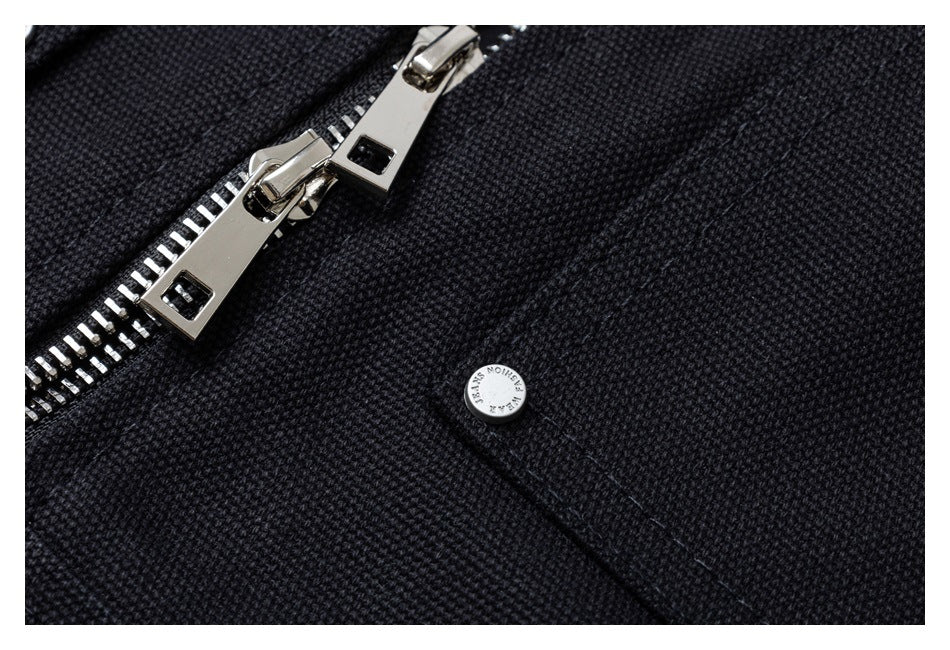 Macro view of the black jacket's silver zipper pulls, textured fabric and a small metal snap.