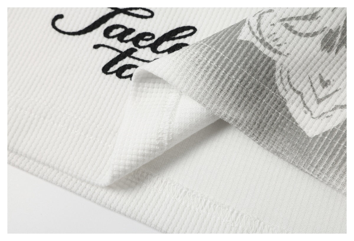 Close-up of the stitched edge of a white ribbed garment beside part of its printed design.