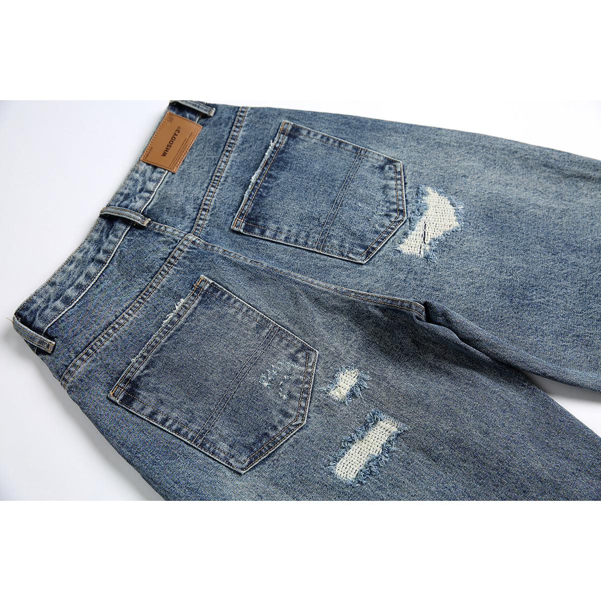 Back of blue acid-wash jeans laid flat, showing two pockets, a leather waistband patch, and distressed patches.