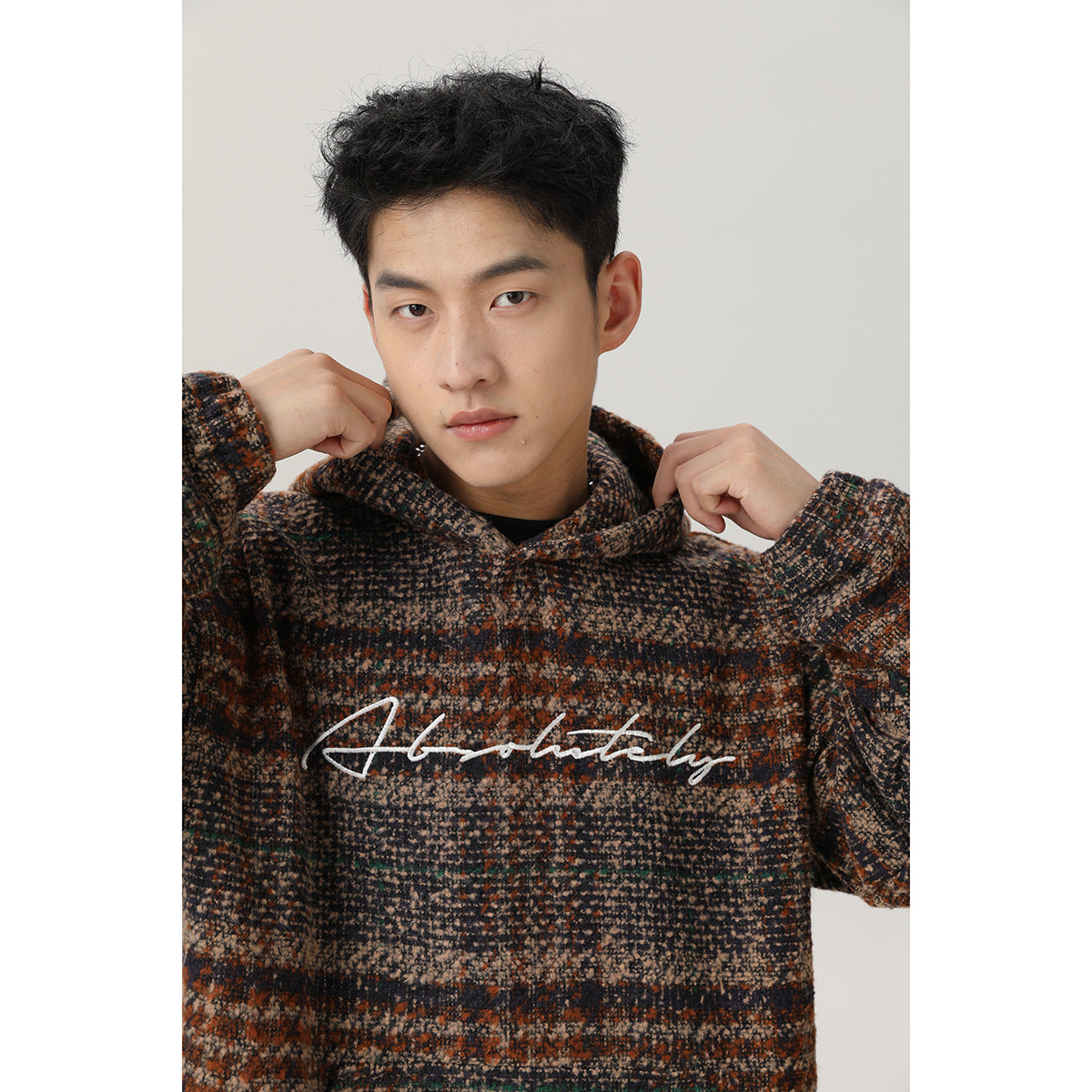 Close view of a man wearing a brown, charcoal and beige striped hooded pullover with white script across the chest.