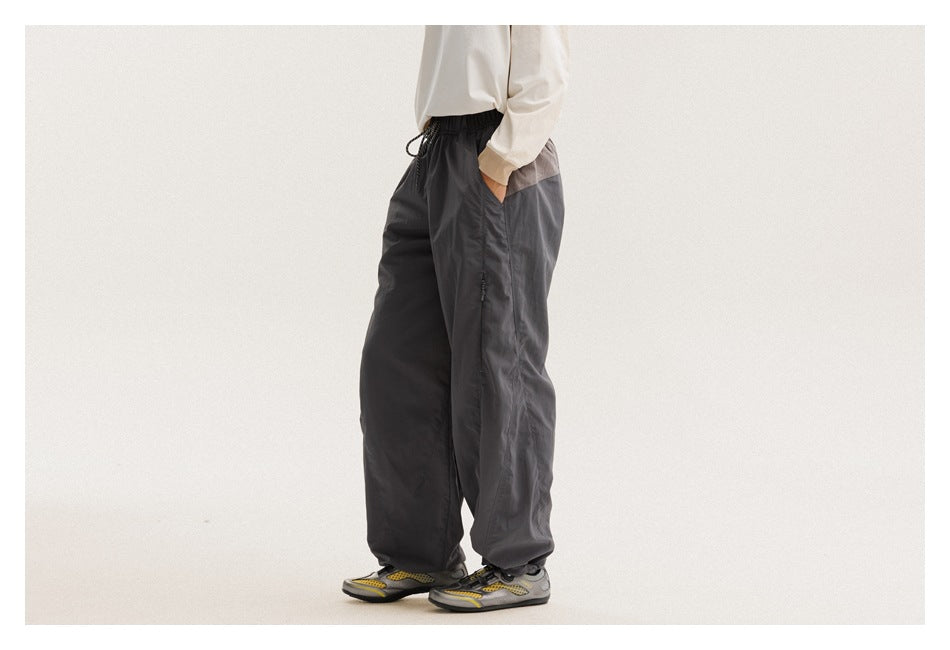 Side view of a model wearing loose charcoal-gray pants with a drawstring waist and a contrasting waistband panel.