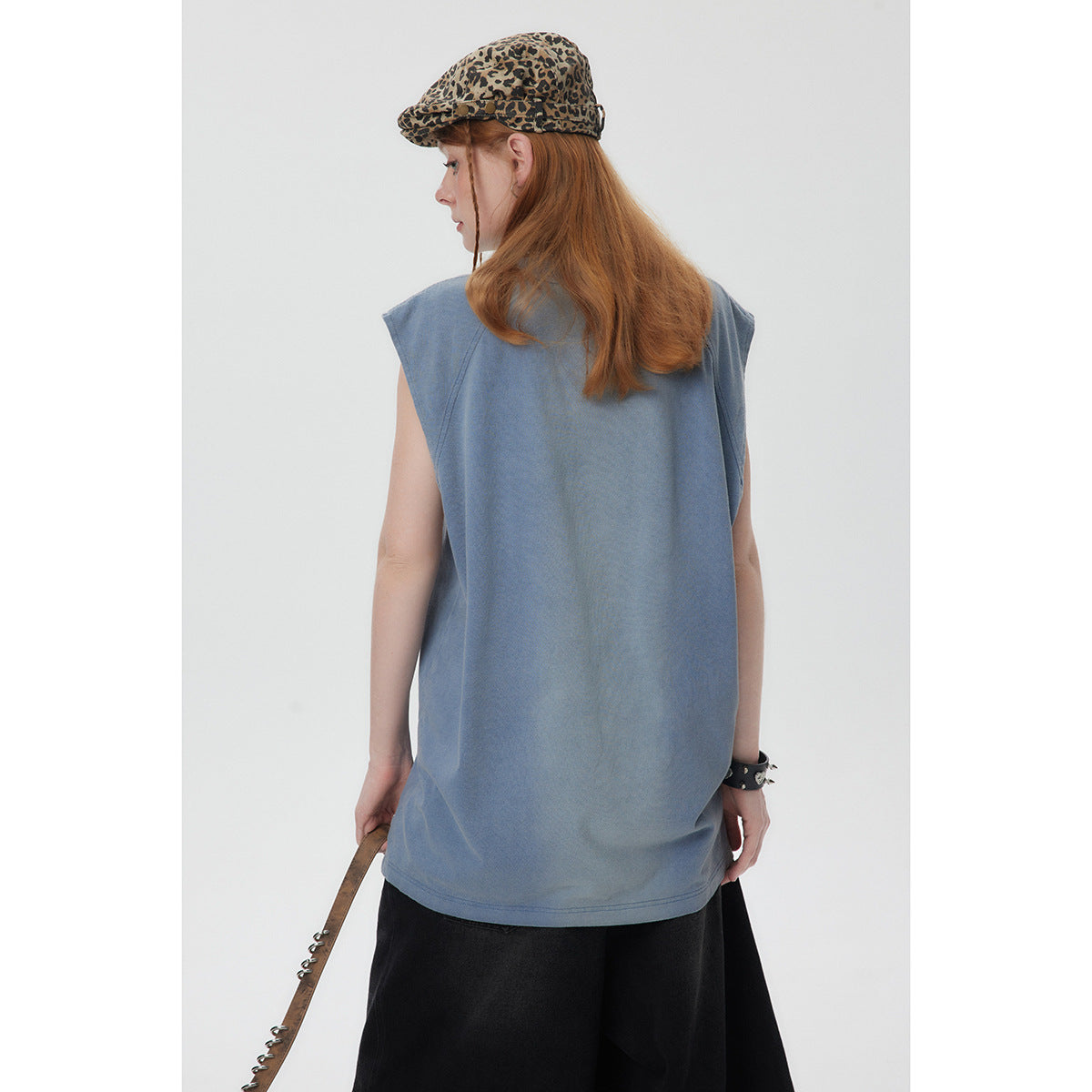 Back view of a model wearing a loose slate-blue sleeveless top with raglan seams and black trousers.