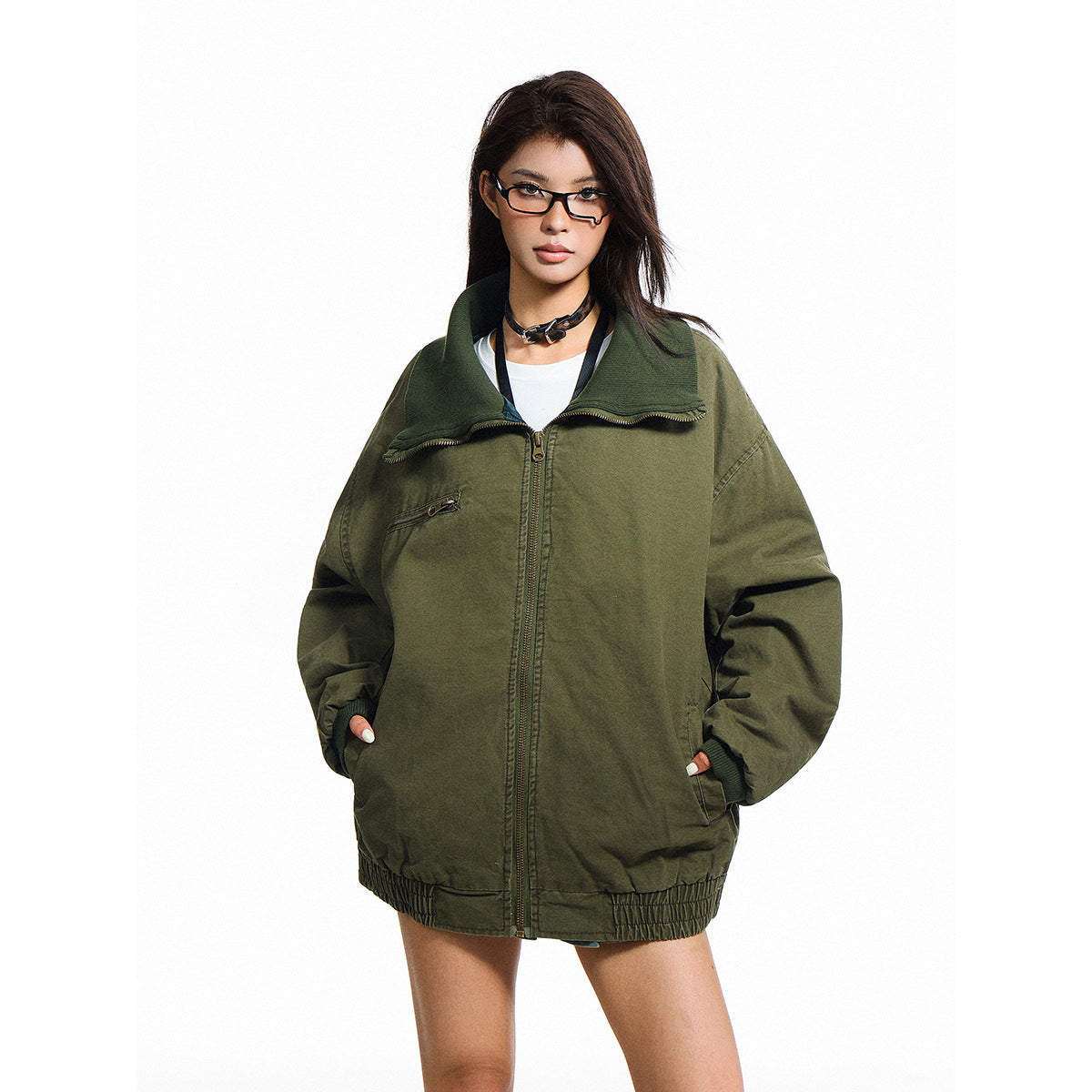 Model wearing an oversized dark olive zip jacket with a wide folded collar, chest zipper pocket and gathered hem.
