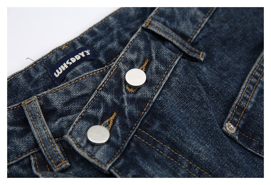 Close-up of dark blue jeans showing the waistband, belt loop, metal buttons and contrast stitching.