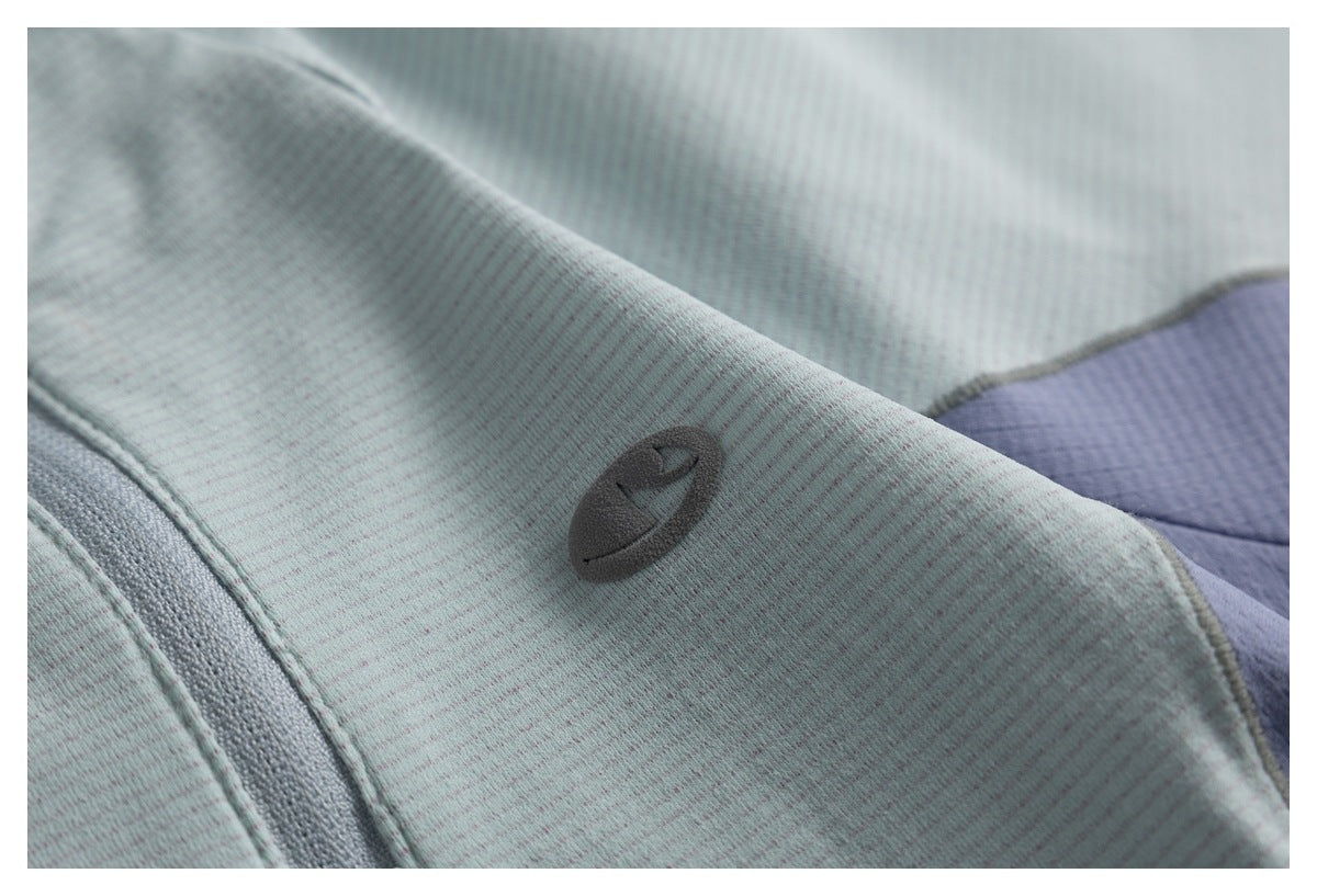 Close-up of a small dark embossed emblem on pale gray-green fabric beside a lavender panel.
