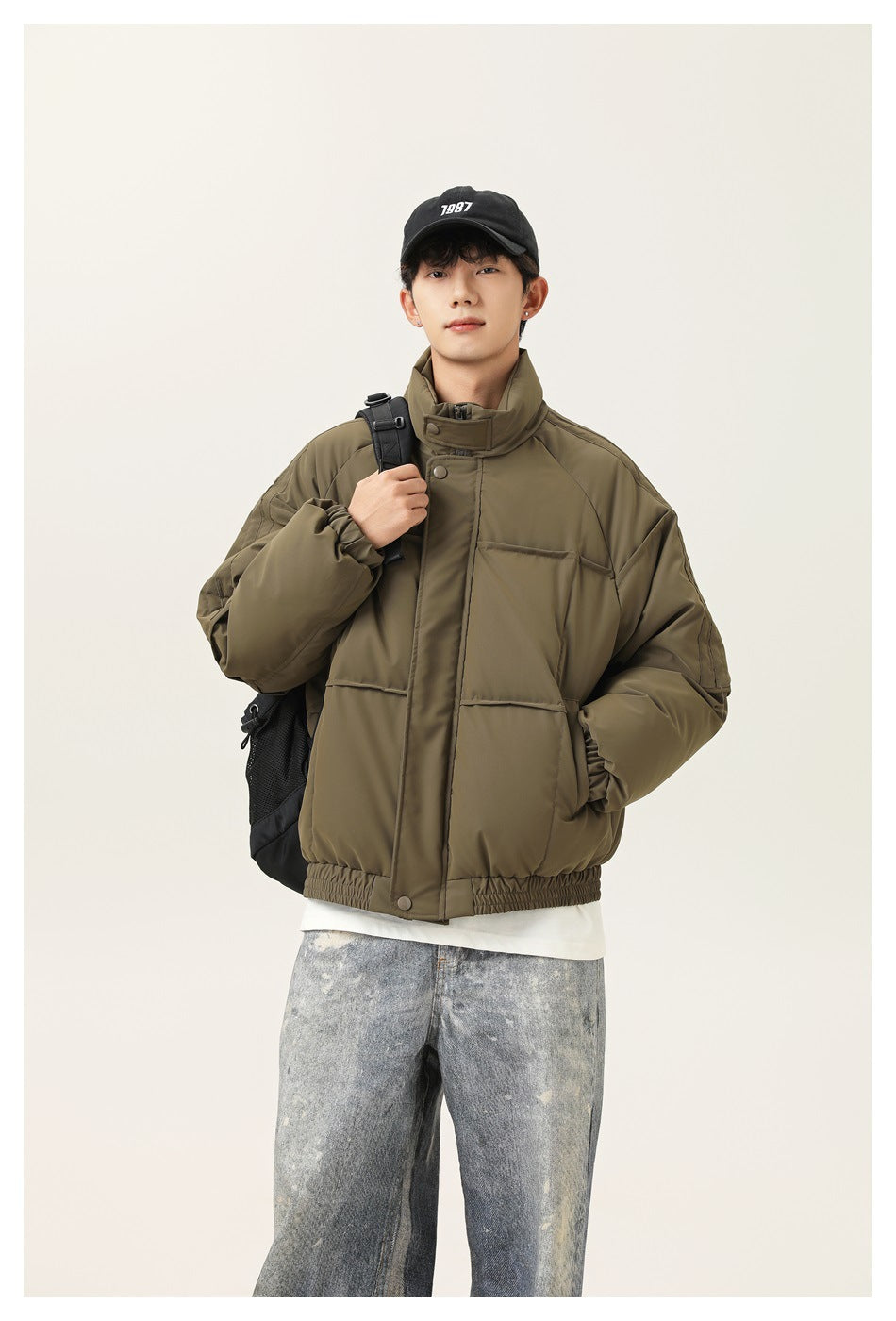 Model wearing an olive green padded jacket with a high collar, front pockets and an elastic hem.