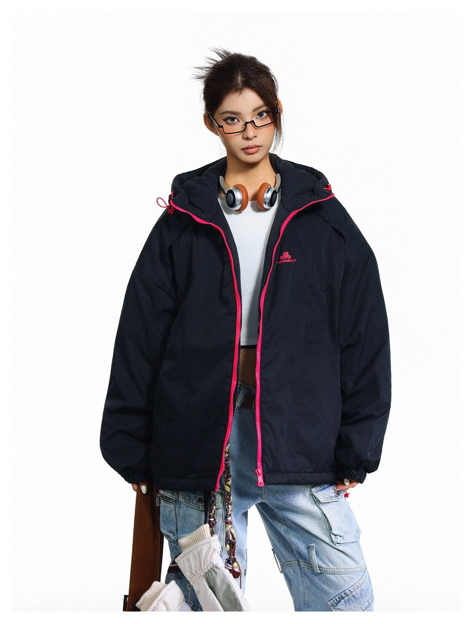Model wearing an oversized black hooded jacket with bright pink zipper trim, open over a white top.