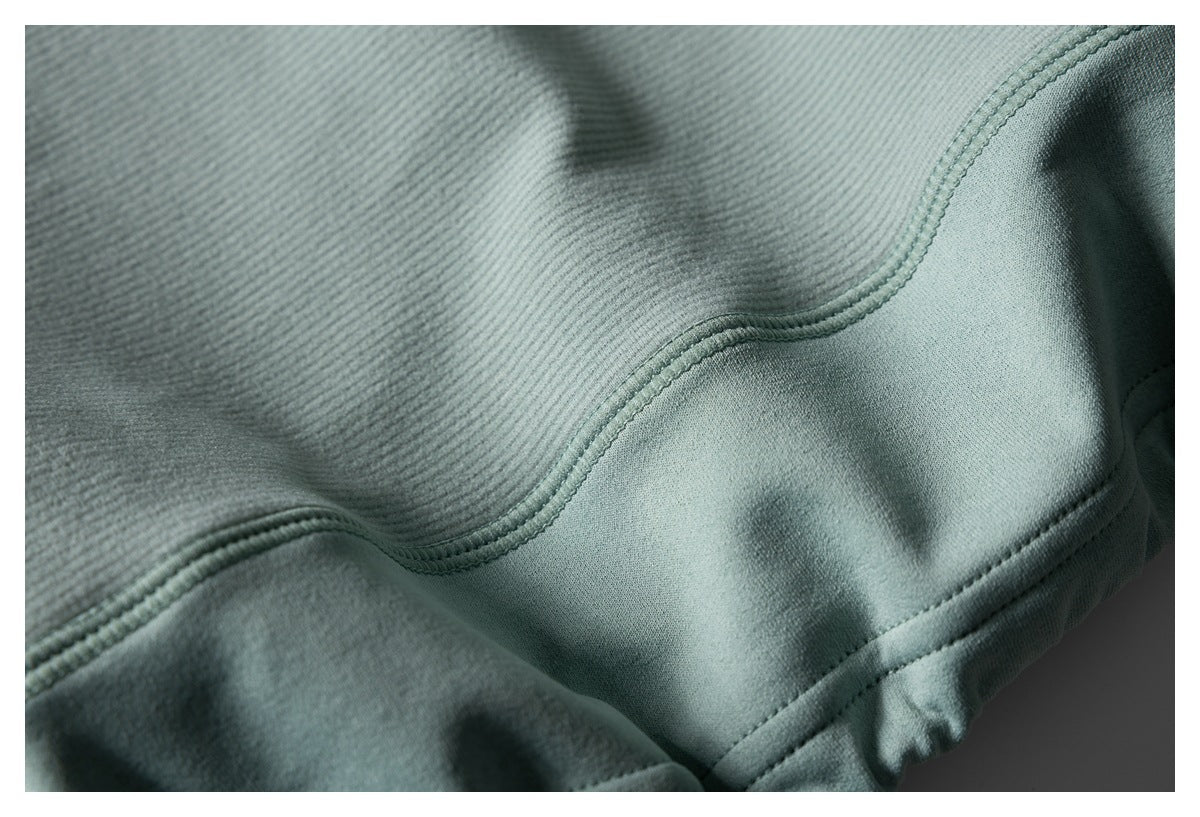 Close-up of sage-gray ribbed fabric showing curved double stitching and a folded hem.