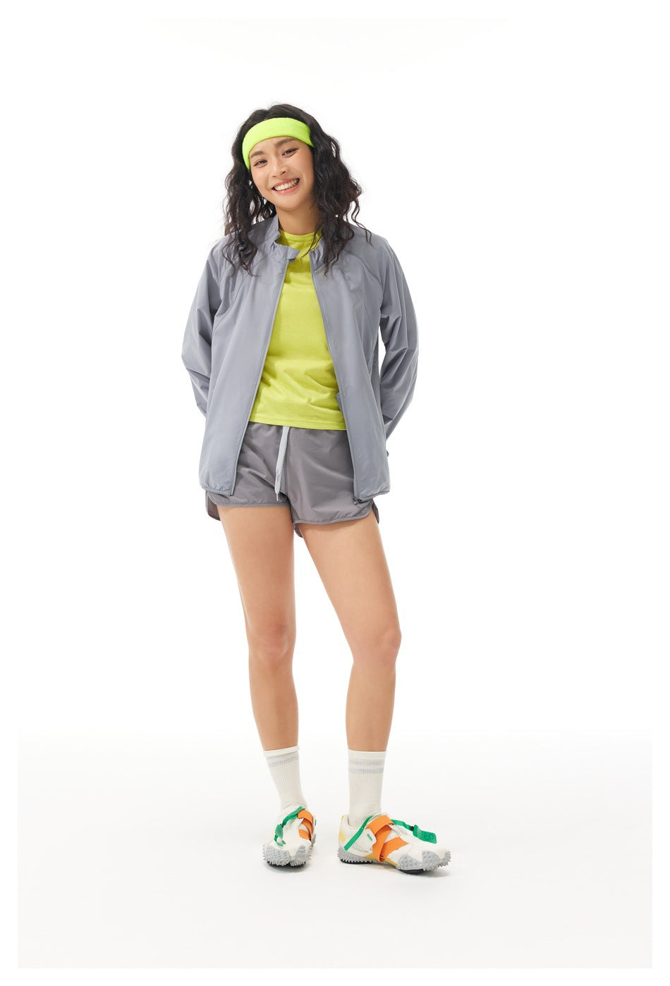 Model wearing a light gray zip jacket and matching shorts over a neon yellow top, with a neon yellow headband.