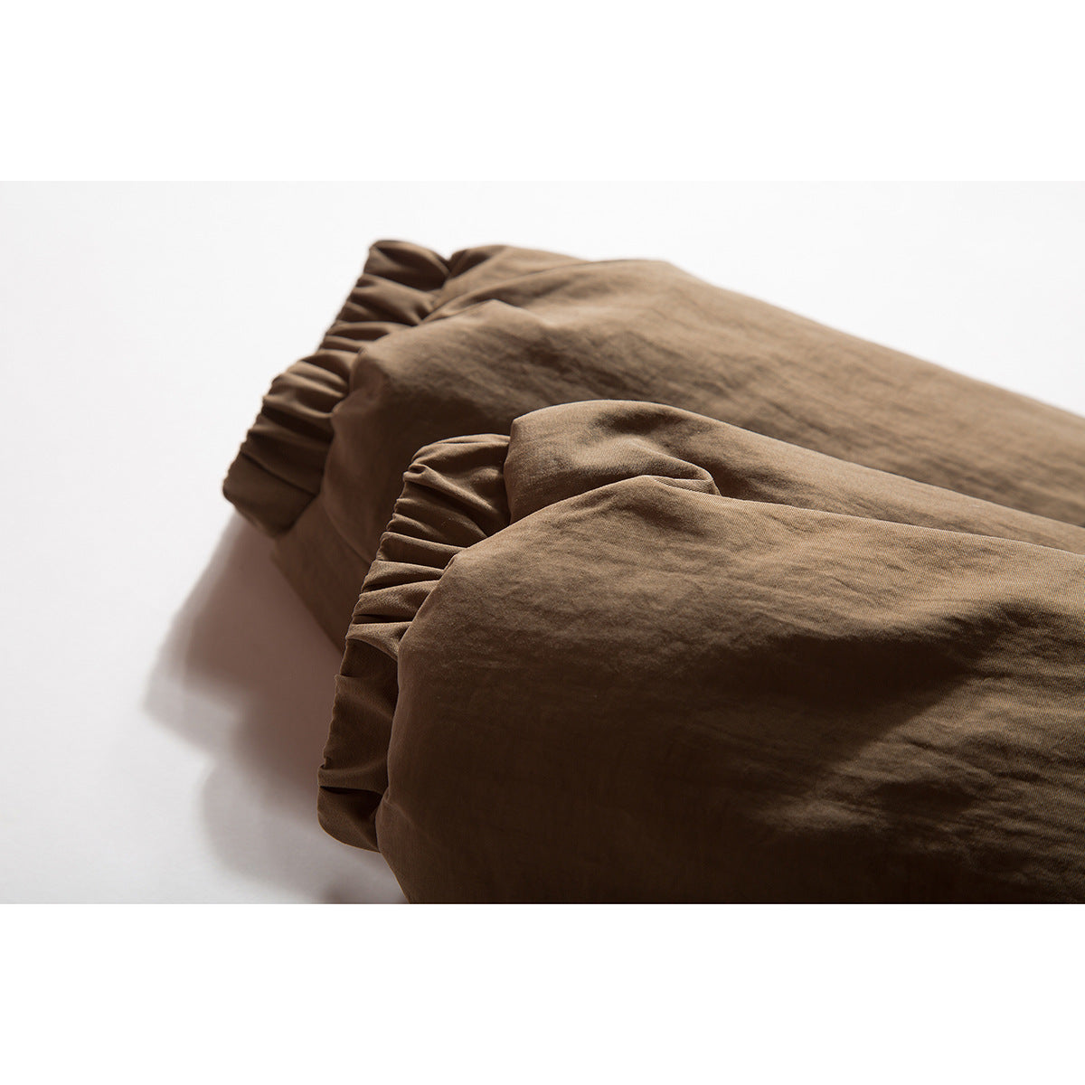 Close-up of two brown garment cuffs with gathered, pleated edges.