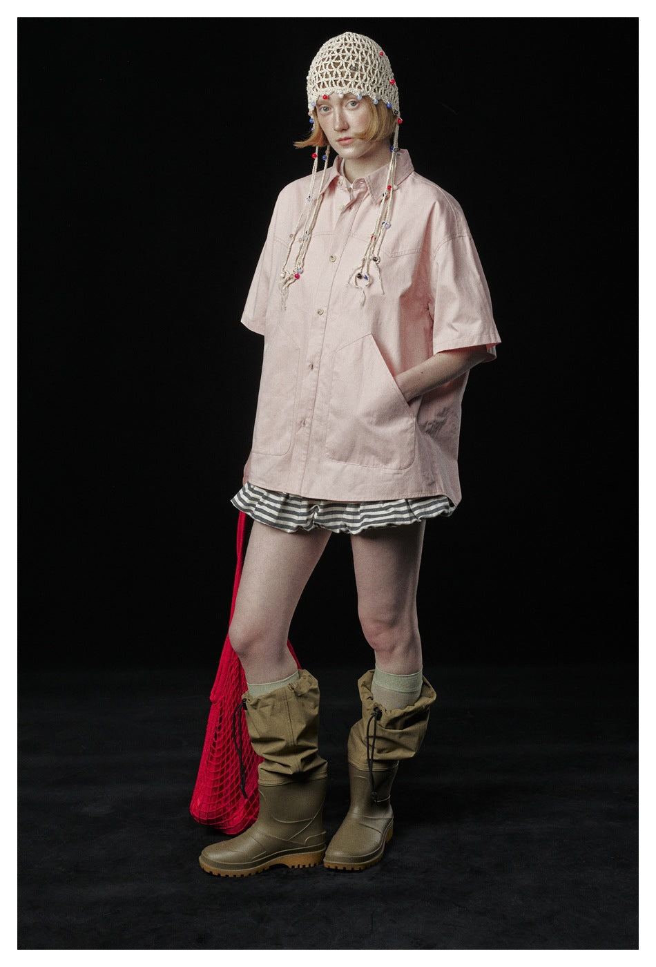 Full-length model wearing a pale pink oversized short-sleeve button-up shirt with striped shorts.