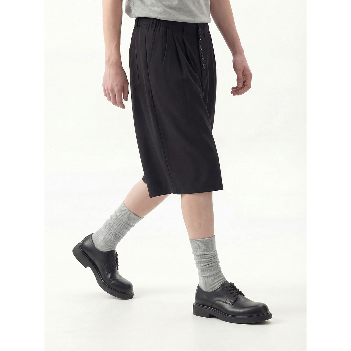 Model wearing black knee-length shorts, shown at an angle with the buttoned waist and side pocket visible.