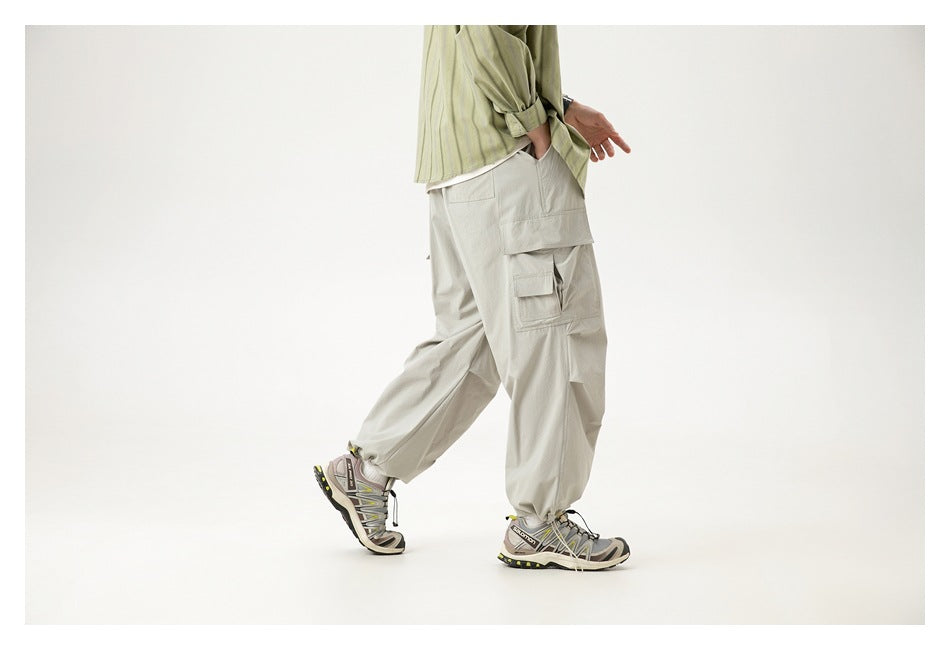 Side rear view of a cropped model walking in loose light gray cargo pants with large layered cargo pockets.