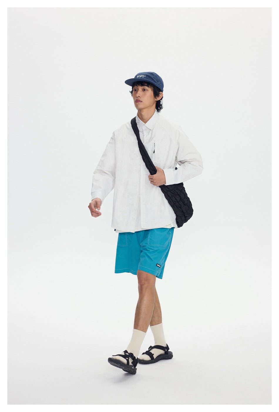Model wearing bright turquoise shorts with patch pockets and contrast stitching, paired with a white shirt.