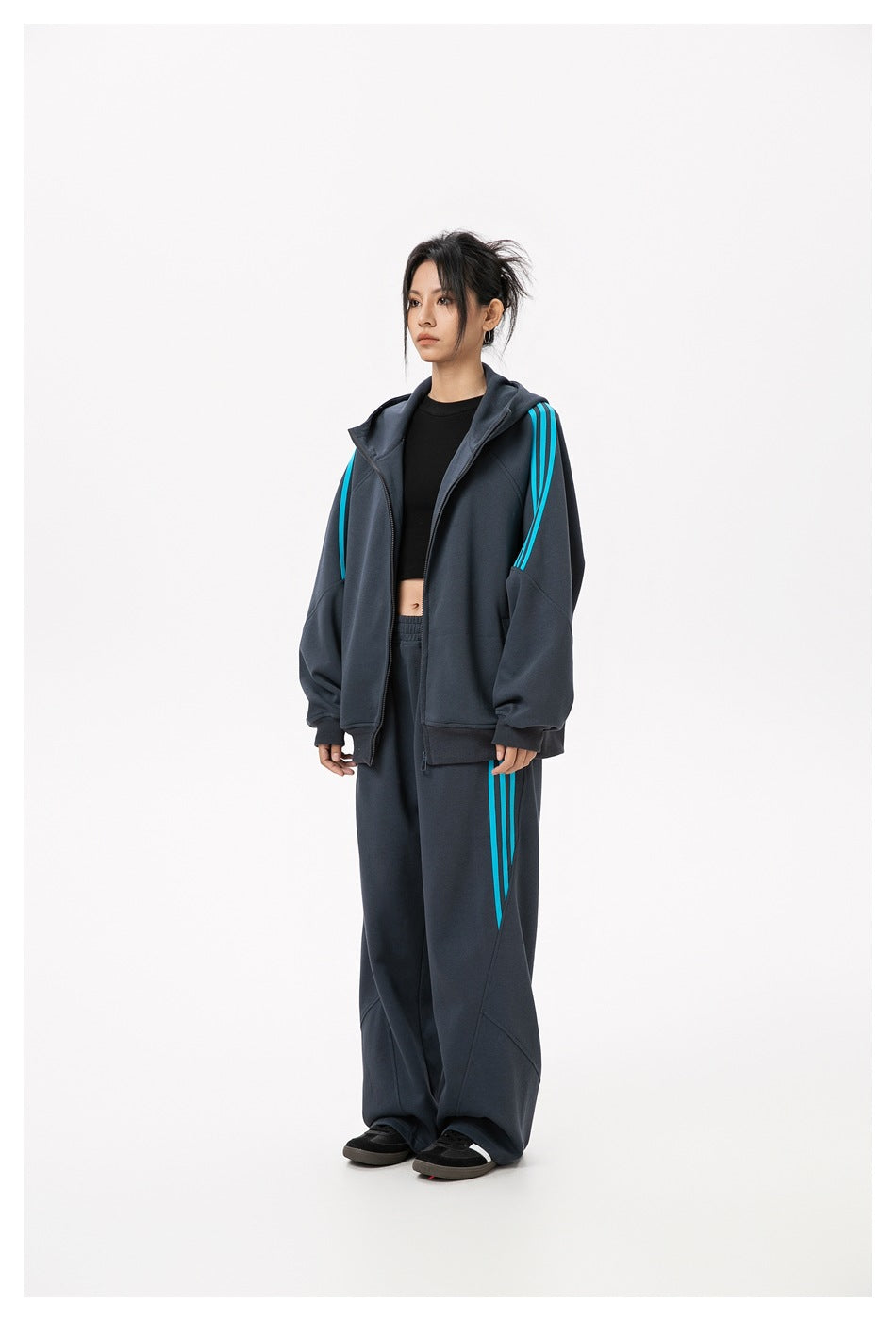 Model wearing an open dark gray striped zip hoodie with a black crop top and matching wide-leg pants