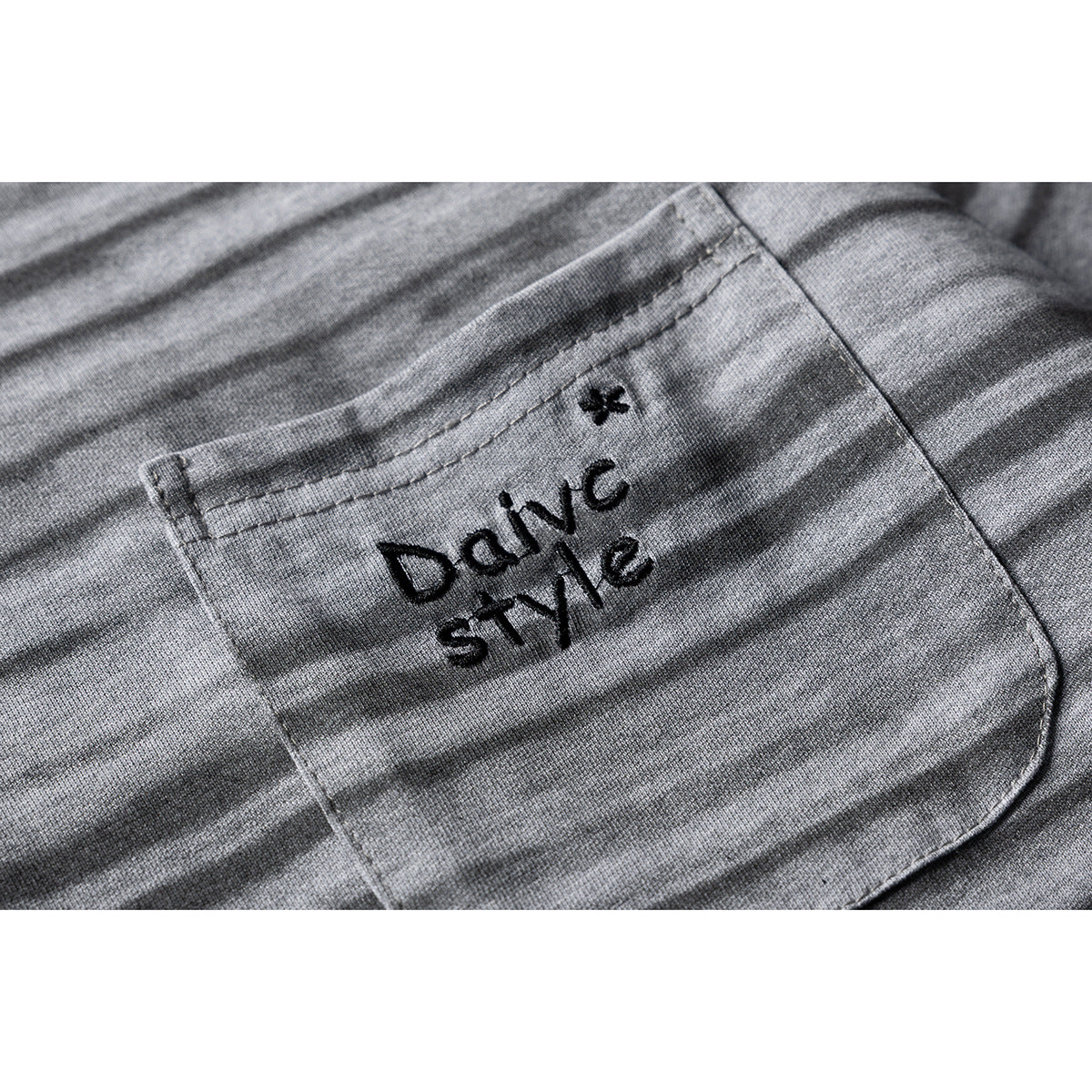 Close-up of a chest pocket on a gray striped T-shirt, with black embroidered lettering.