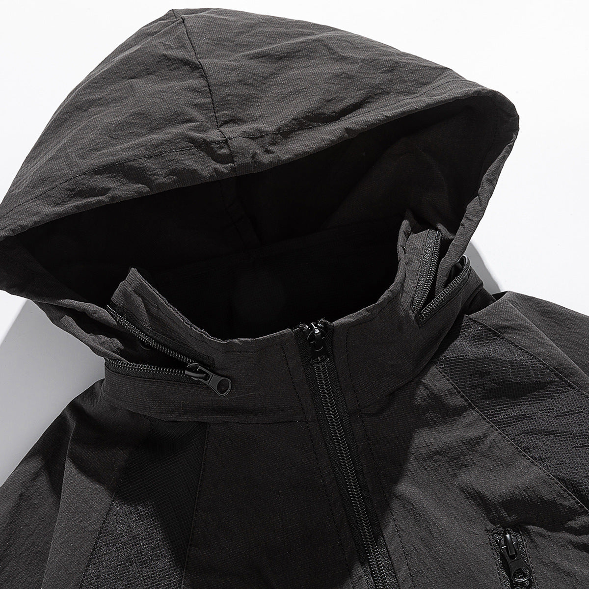 Close-up of a black hooded jacket showing the hood, high zip collar, front zipper and pocket zippers.