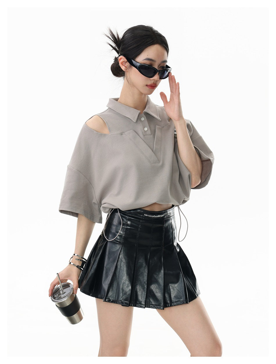 Model wearing a taupe cutout-shoulder polo top with a V-shaped front panel and drawstring hem, paired with a black pleated