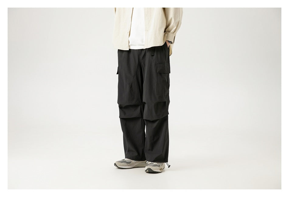 Person wearing black cargo pants with a beige shirt and gray sneakers, angled view, cropped at the torso