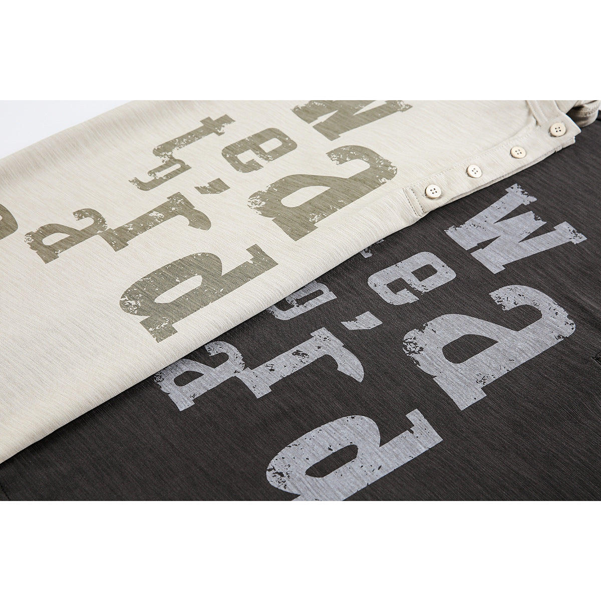 Close-up of beige and charcoal T-shirts with distressed graphic lettering and button plackets.