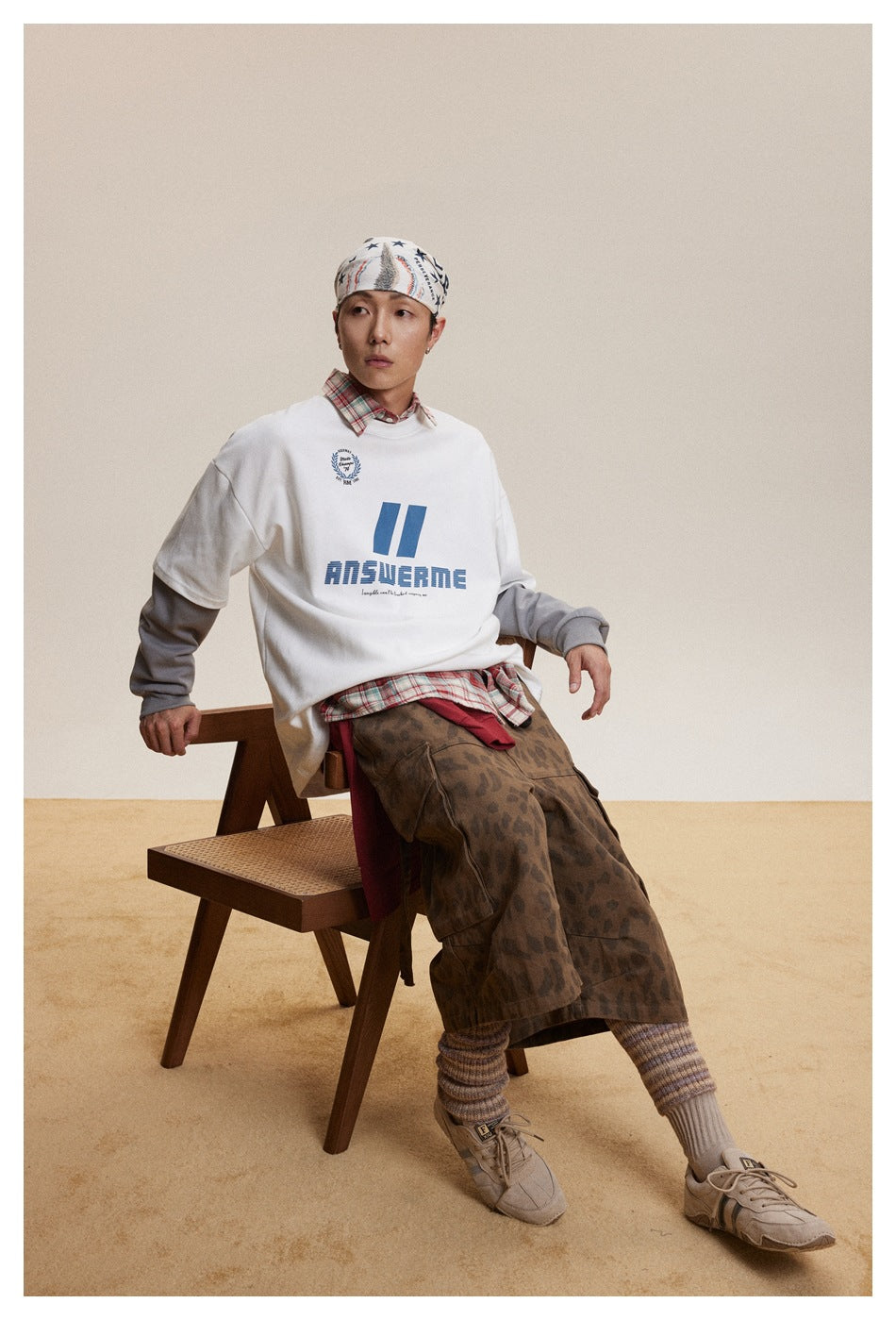Seated model wearing a white sweatshirt with blue chest graphics and gray layered sleeves.