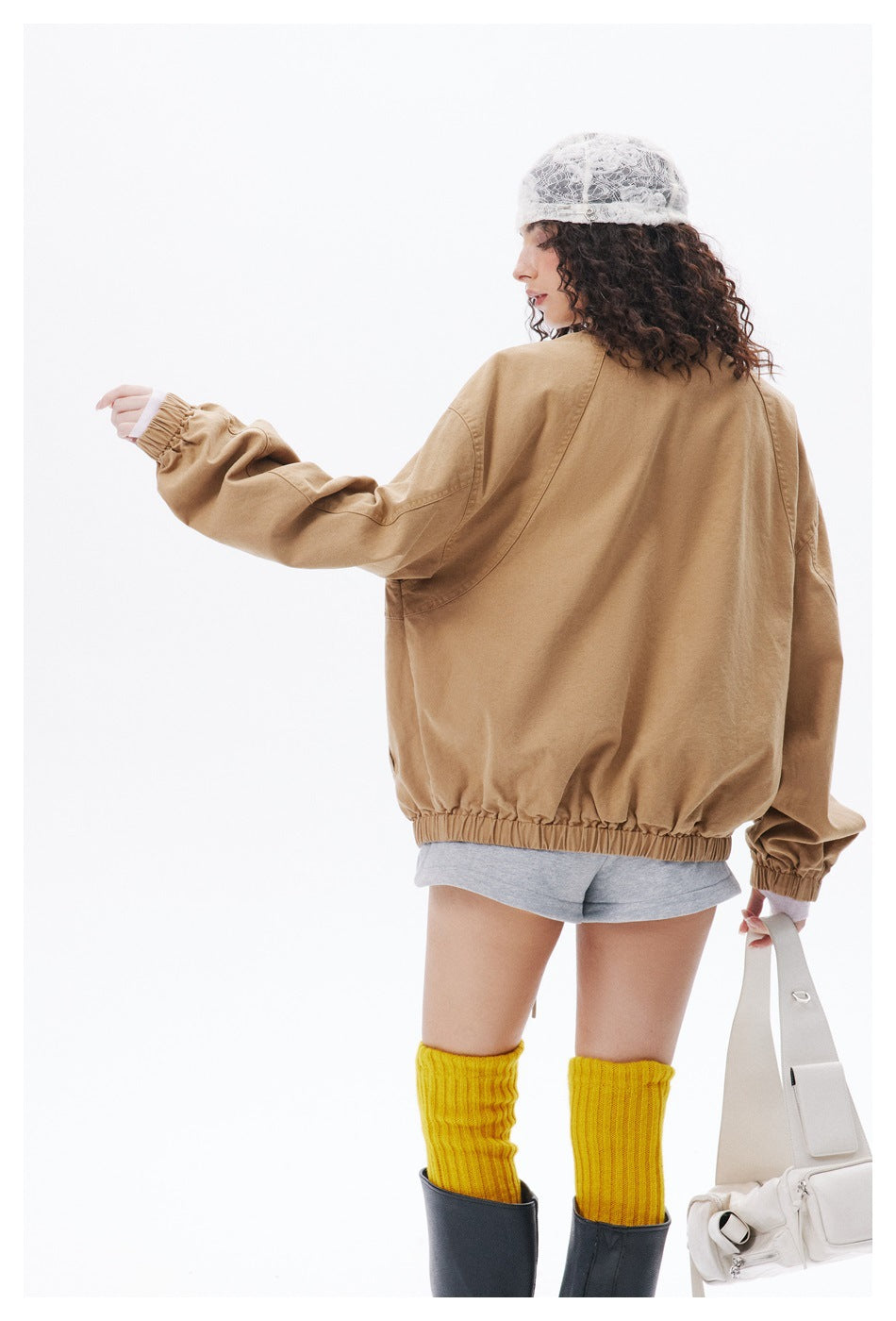 Rear view of a model wearing an oversized tan jacket with a high collar, dropped shoulders, and elasticated hem and cuffs.