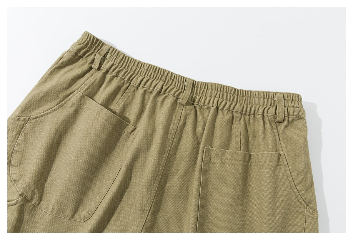 Close-up of olive-khaki trousers showing the elastic waistband, belt loops, and large front pockets.