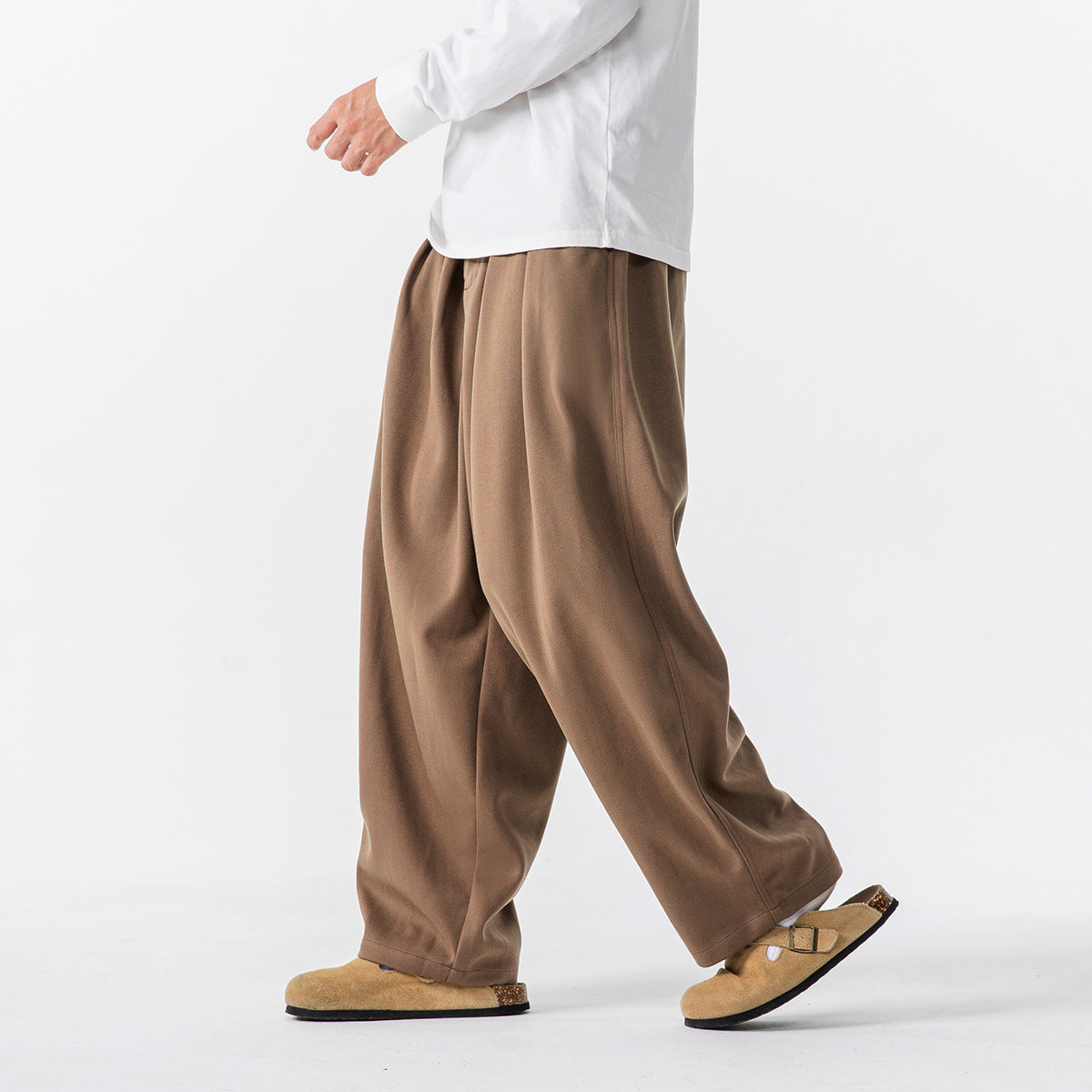 Side view of a person walking in loose brown trousers and a white long-sleeve shirt.