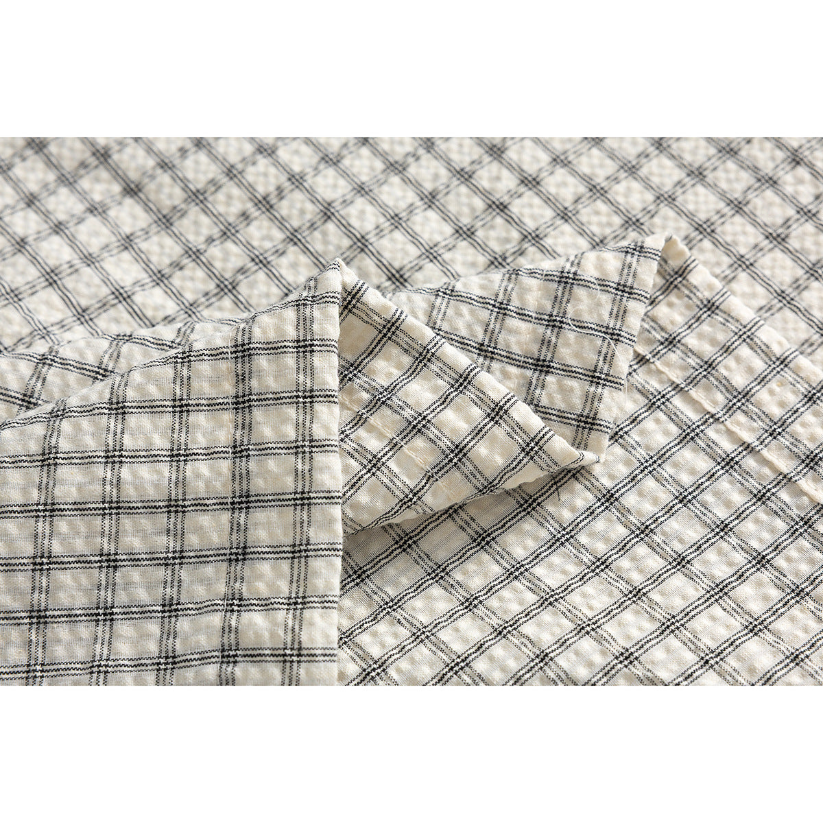 Close-up of the cream shirt's black grid plaid pattern and textured, folded fabric.