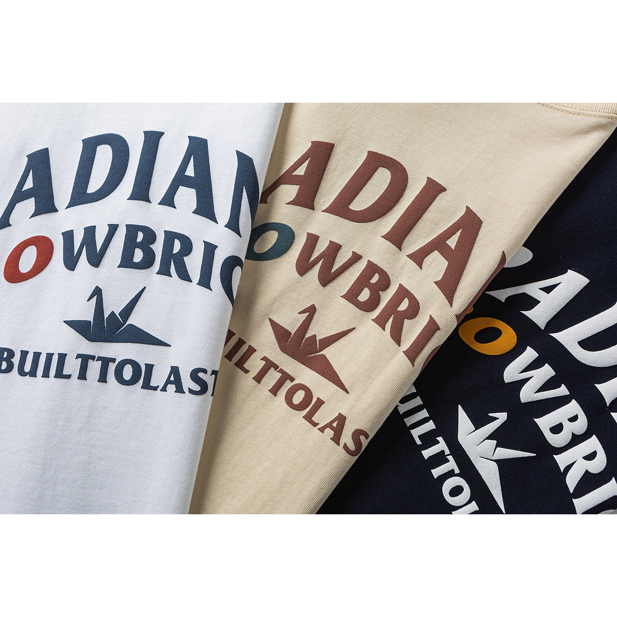 Close-up of white, cream, and navy T-shirts with large multicolor printed lettering and graphics.