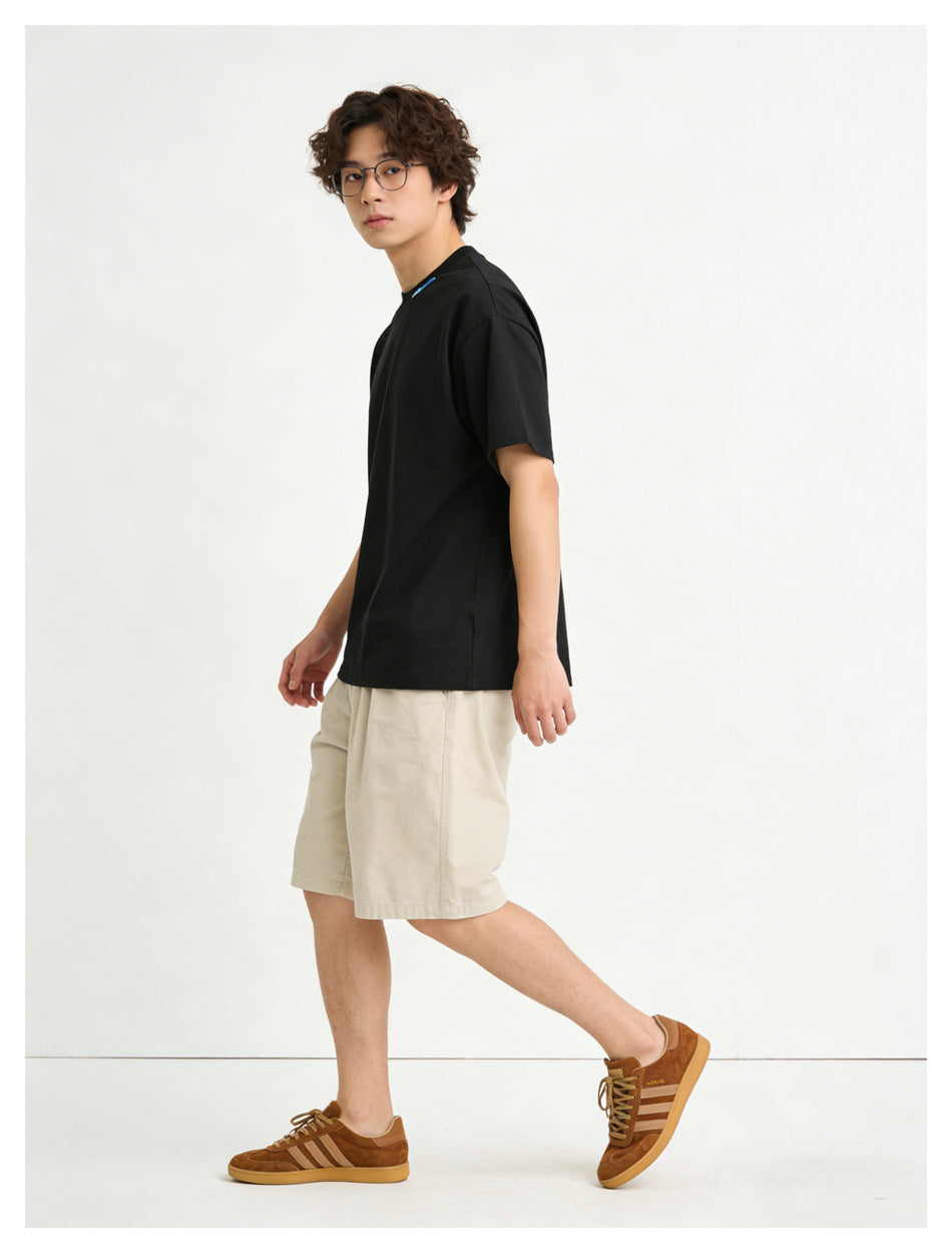 Side view of a model wearing a black short-sleeve T-shirt with a small blue neckline detail and light beige shorts.
