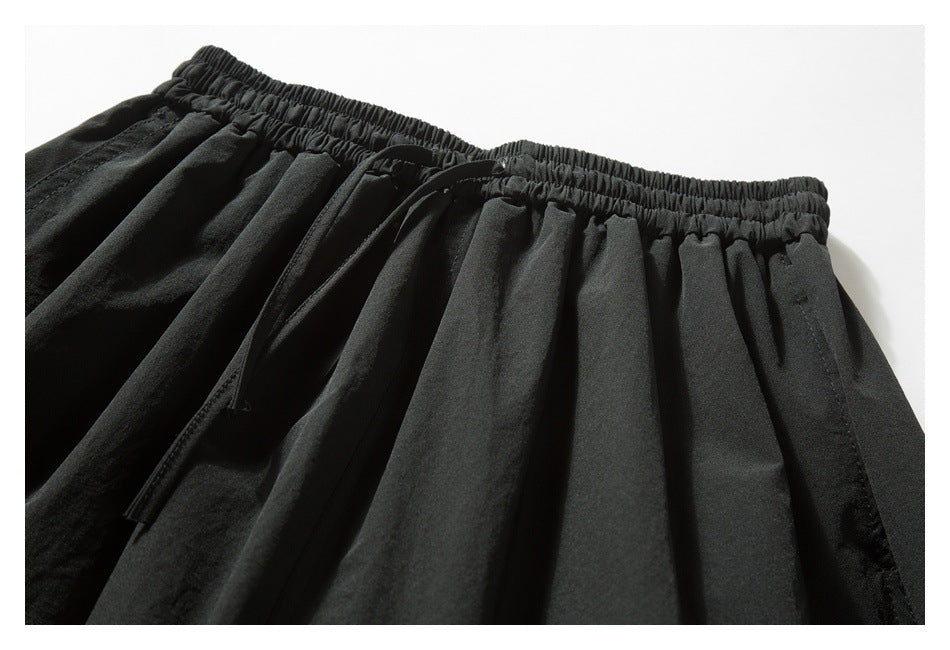 Black garment detail showing a gathered elastic waistband, drawstring, and pleated fabric.