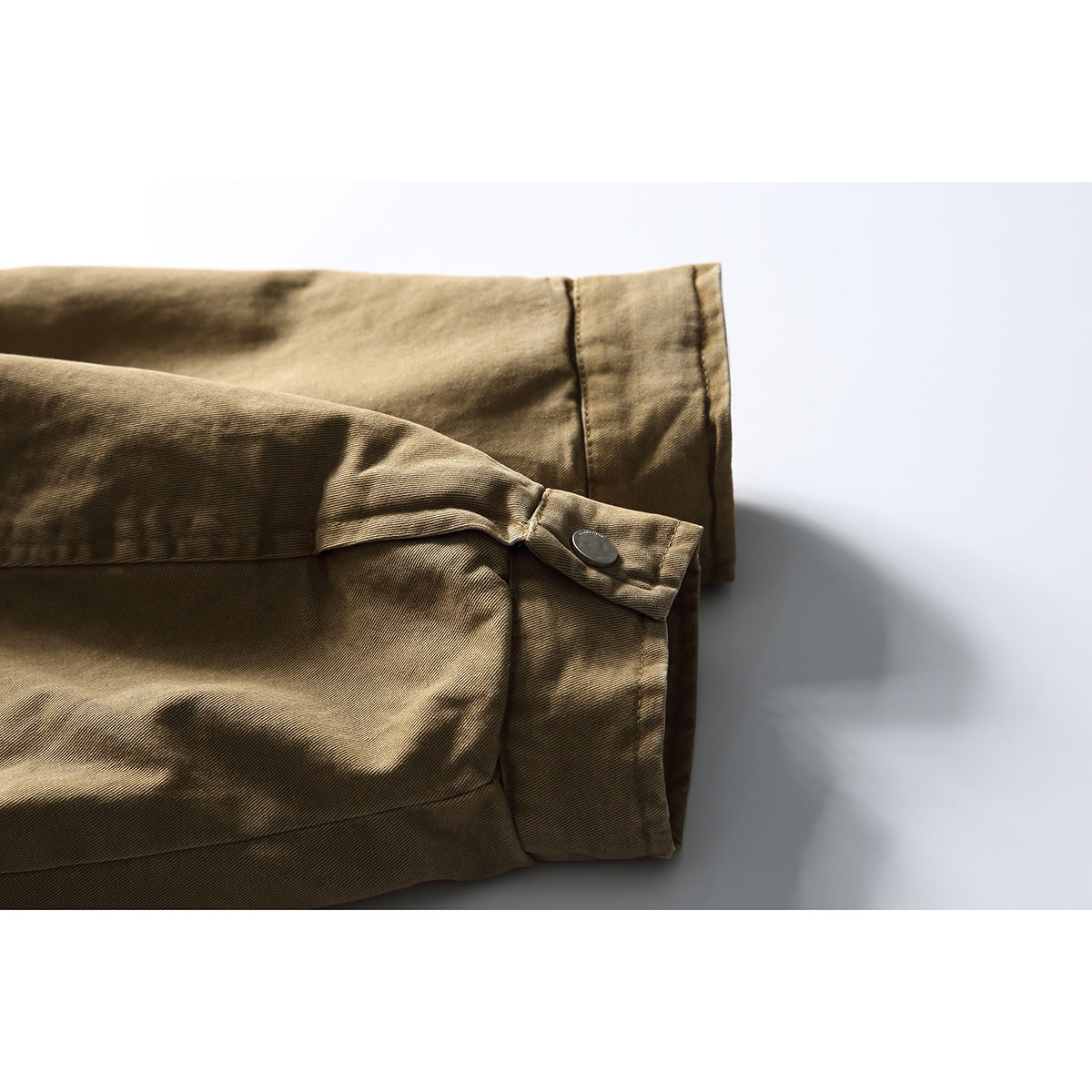 Close-up of a tan jacket sleeve cuff with a buttoned tab and visible stitching.