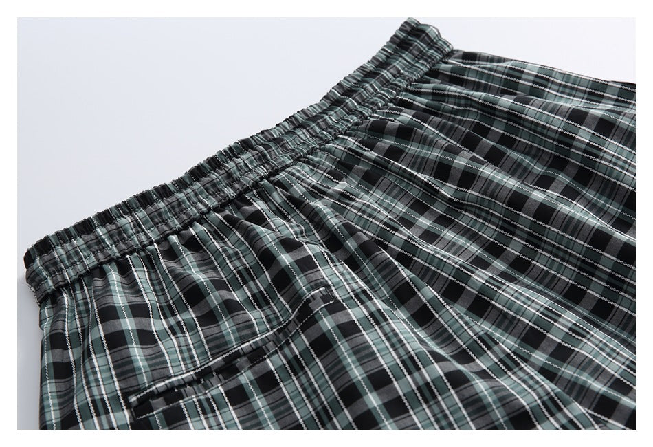 Close-up of the elastic waistband and rear pocket on black, gray, and muted green plaid trousers.