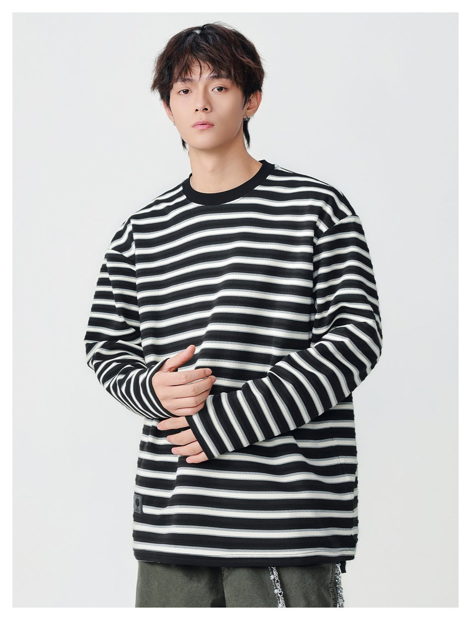 Model wearing an oversized black, gray, and white striped long-sleeve shirt with a black crew neck; front view.