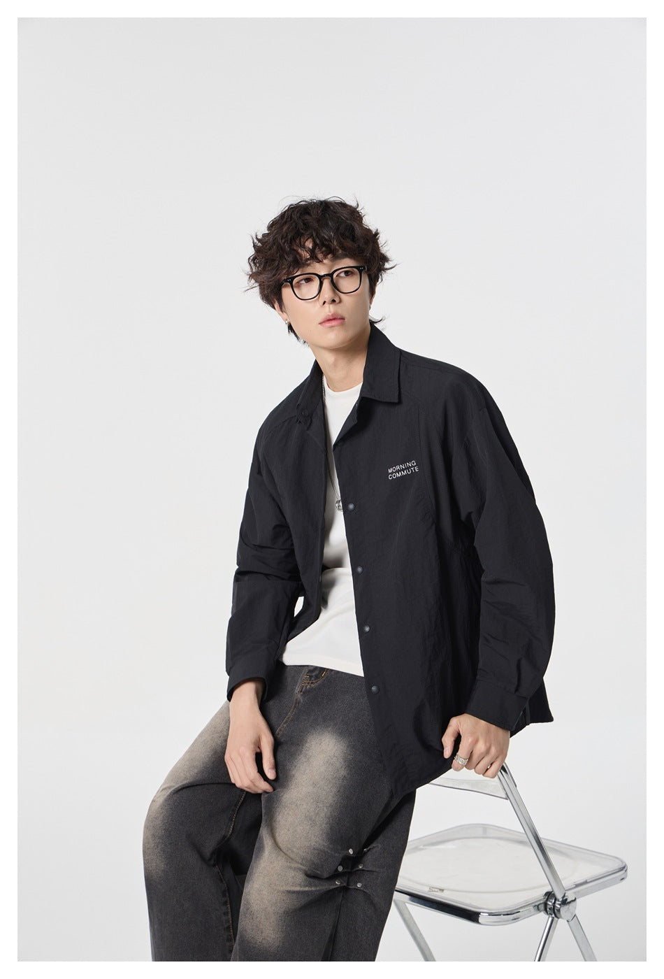 Seated model wearing a black button-front overshirt over a white tee with washed dark jeans.