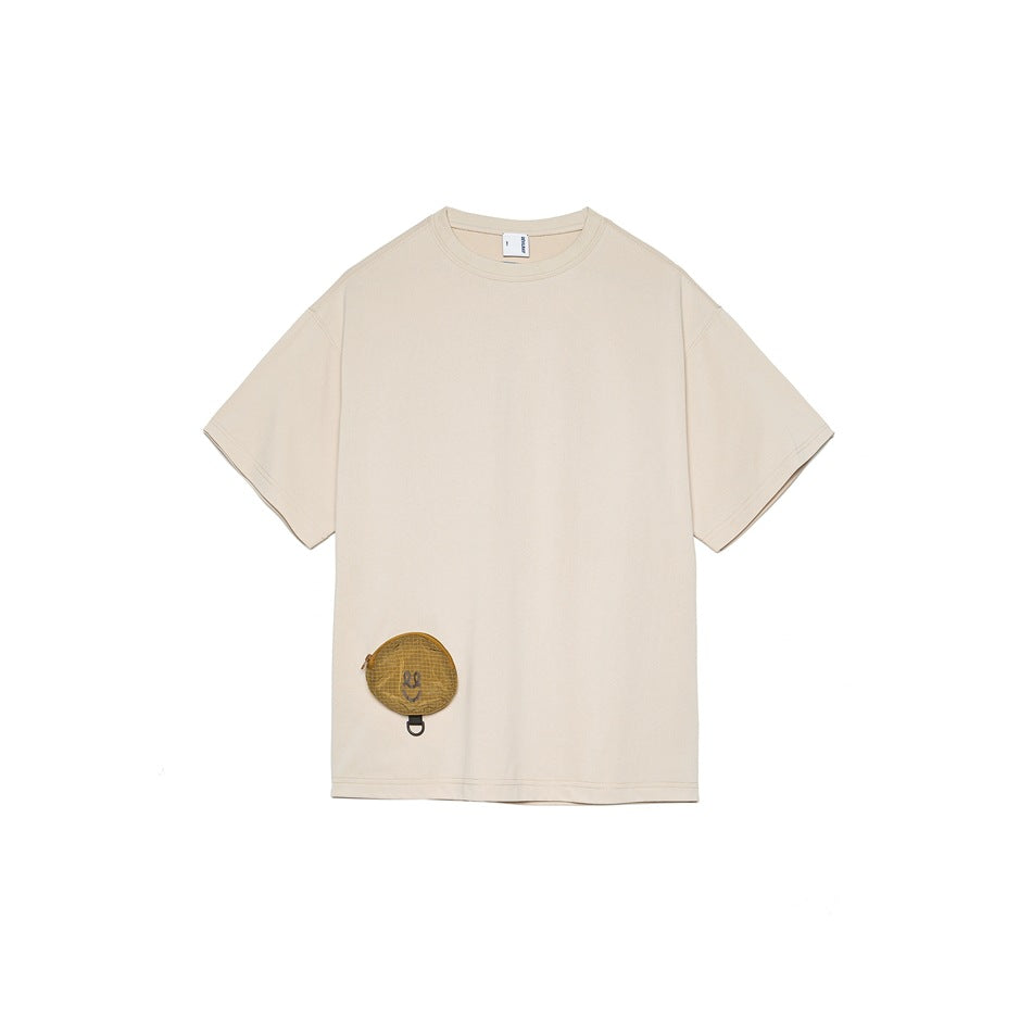 Light beige short-sleeve crew neck t-shirt with a small yellow mesh smiley pouch at the lower front hem