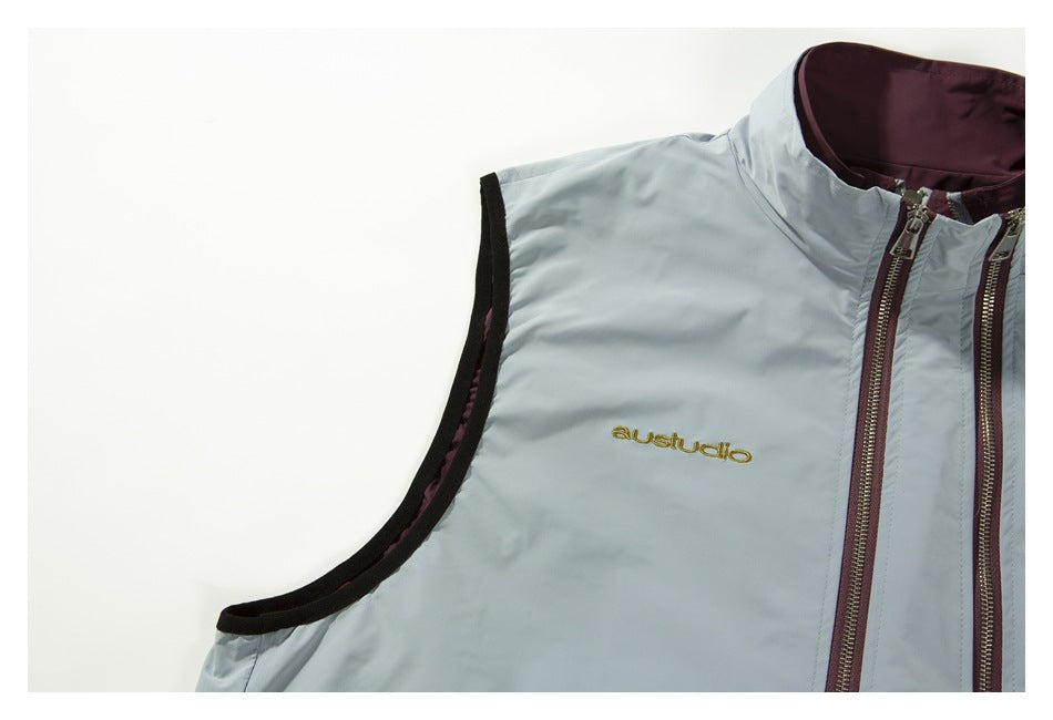 Close-up of the vest’s pale gray front, black armhole trim, plum lining, zippers, and gold embroidered logo.