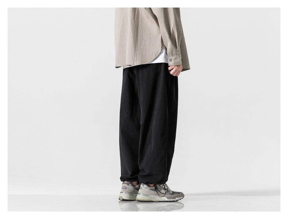 Model wearing loose black trousers with gathered hems, shown from the side with gray sneakers.