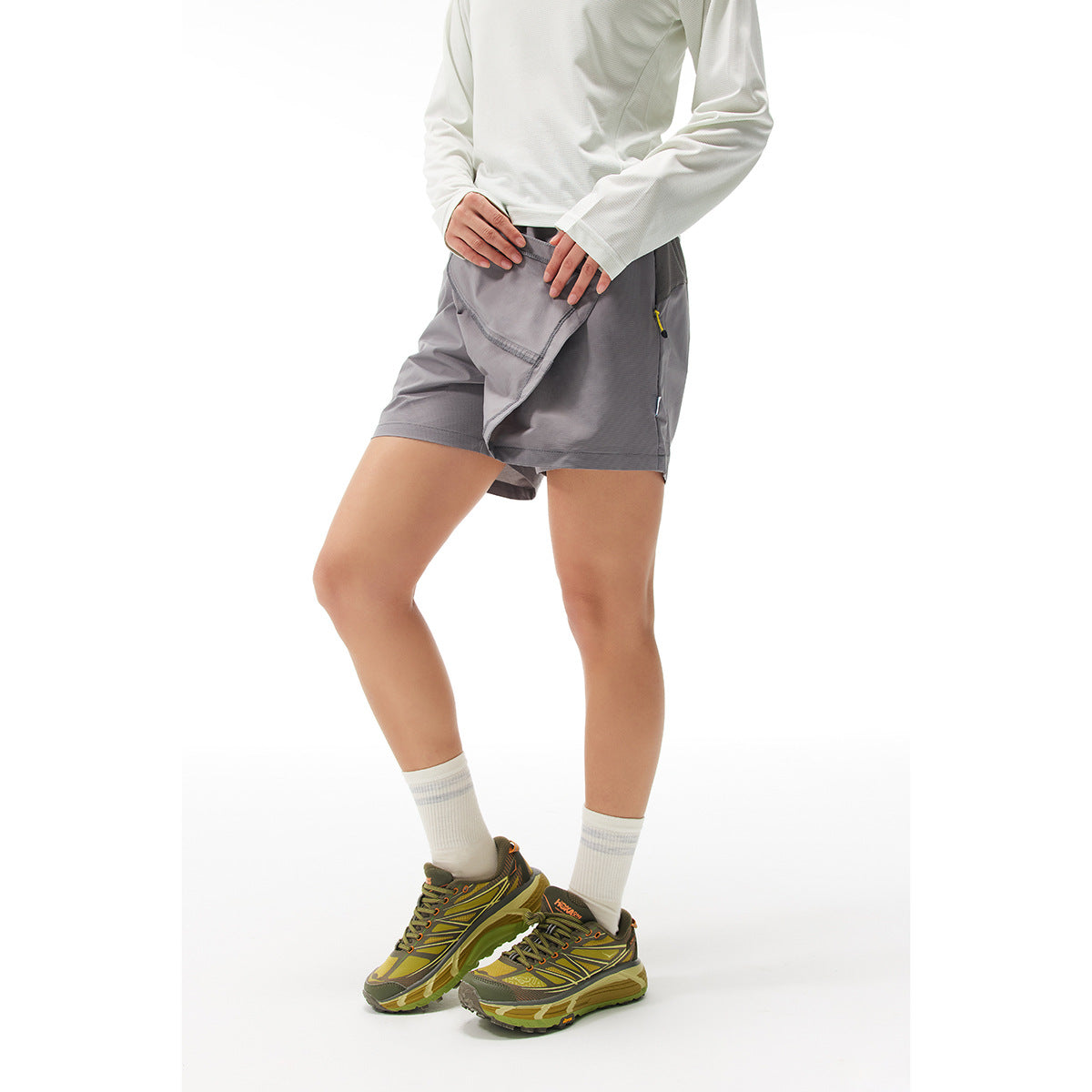 Model wearing gray athletic shorts with an overlapping front panel and zip pockets, shown from the front.