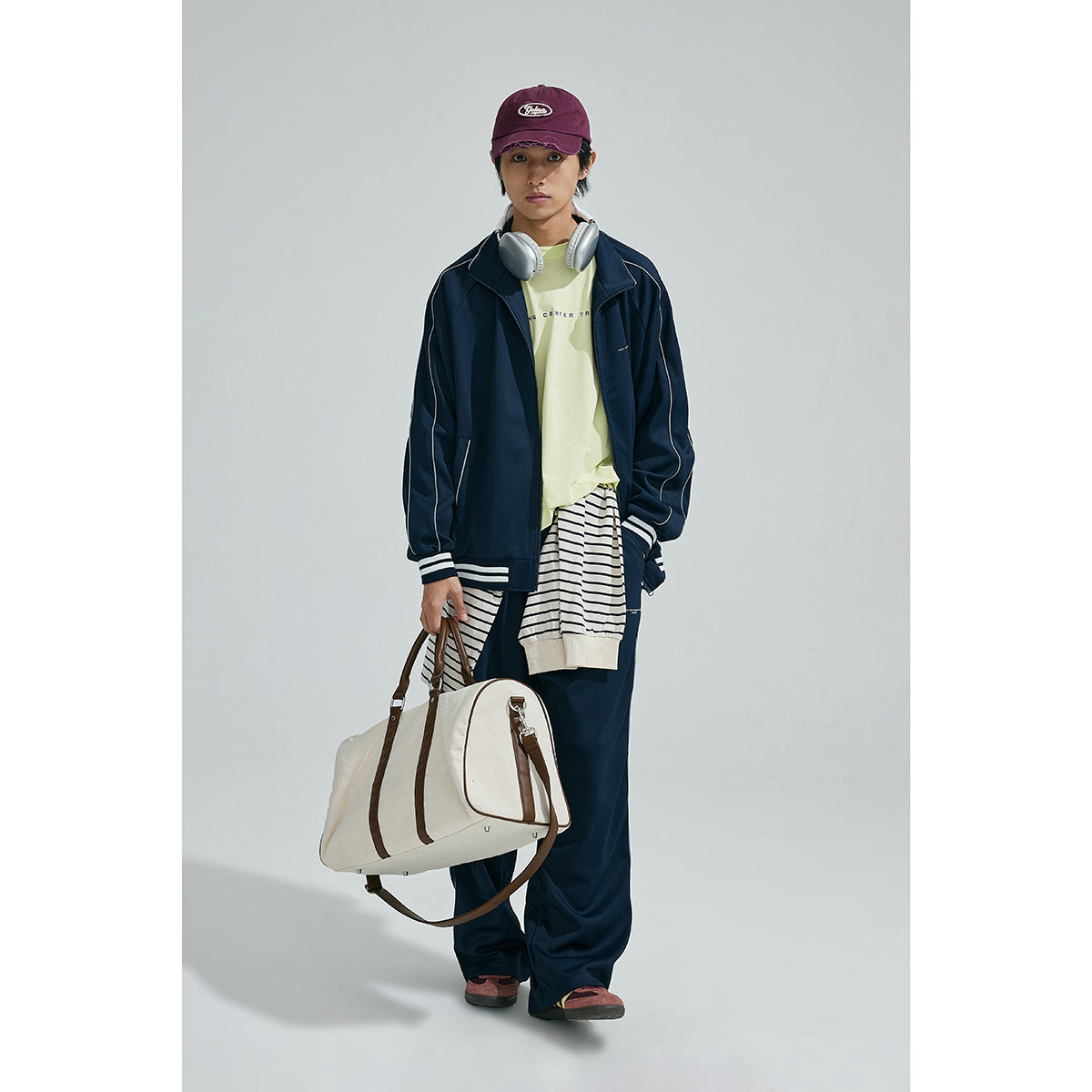 Full-length front view of a model in a navy tracksuit jacket and pants with white piping and striped layers.
